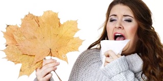 生病的女人用纸巾捂着秋叶打喷嚏