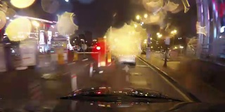 快速城市行驶夜间道路POV时间推移的挡风玻璃和车罩，雨夜，雨滴在玻璃上