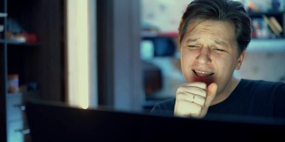 一个男人一边在笔记本电脑上工作一边唱歌。