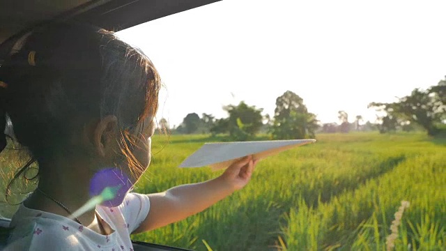 可爱的小女孩在乡下玩着玩具纸飞机窗外。晚上放松的活动概念。Slowmotion拍摄