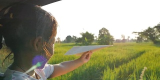 可爱的小女孩在乡下玩着玩具纸飞机窗外。晚上放松的活动概念。Slowmotion拍摄
