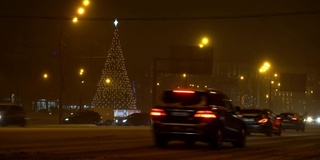 圣诞树在夜晚城市冬天积雪覆盖的道路上闪闪发光，在交通堵塞的车辆中驶过，概念圣诞夜，新年，雪花，吹暴风雪，汽车覆盖的雪，雪花在车灯