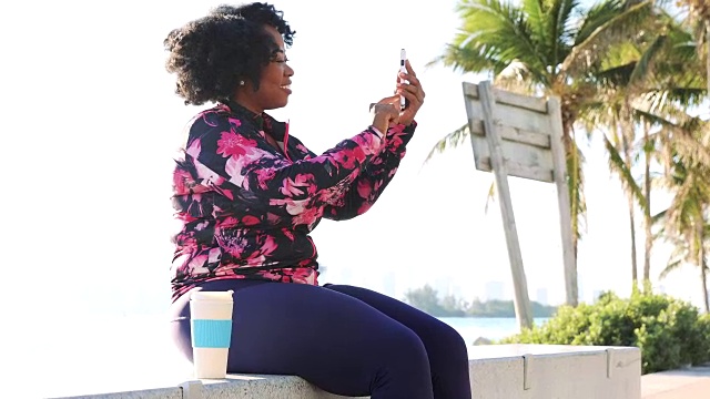 身材婀娜的年轻黑人女性在健身过程中休息，用手机聊天