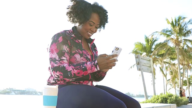 身材婀娜的年轻黑人女性在健身过程中休息，用手机聊天