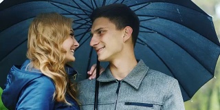 一对年轻夫妇站在一把伞下:在下雨