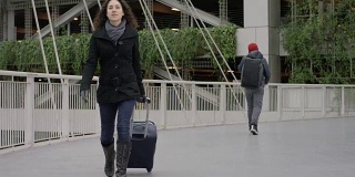 年轻的少数民族女性拉着她的行李箱穿过机场天桥