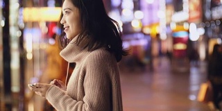 年轻的亚洲女人晚上在街上用智能手机