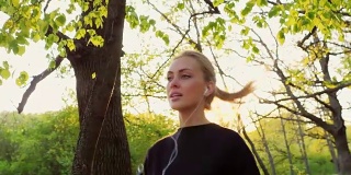 斯坦尼康慢镜头:健康的生活——一个女人在春天的森林里慢跑，听着音乐