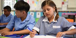 澳大利亚土著女学生穿着格子裙在课桌上写课本