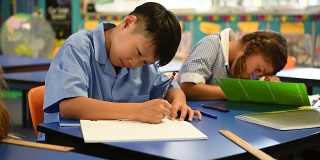 亚洲男孩坐在书桌上写他的教科书