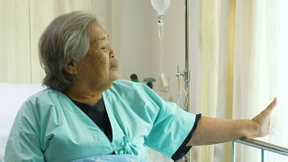 老年妇女坐在病床上和躺在医院里，悲伤的残疾人在病床上感到孤独。退休妇女独自在诊所里。视频素材模板下载