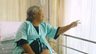 老年妇女坐在病床上和躺在医院里，悲伤的残疾人在病床上感到孤独。退休妇女独自在诊所里。视频素材模板下载
