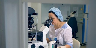 一个穿着手术服的女人正在使用实验室的显微镜。