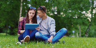 年轻女孩和一个男孩在公园里用平板电脑，男孩拥抱女孩