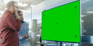 男、女在会议室讨论彩色键绿屏电视样机。