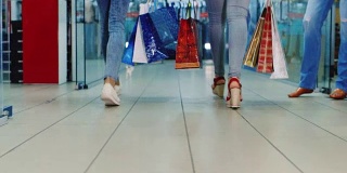 两个女人拿着购物袋在购物中心。后视图，只有腿可见