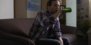 醉汉坐在沙发上，看着啤酒瓶，打嗝，喝酒