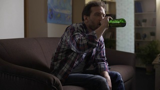 醉汉坐在沙发上，看着啤酒瓶，打嗝，喝酒视频素材模板下载