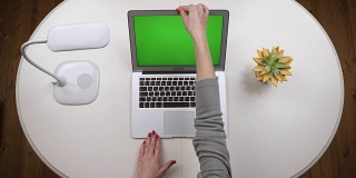 女人打开笔记本电脑，站在有灯的白色桌子上，输入文字，然后关上笔记本电脑。前视图。手关闭