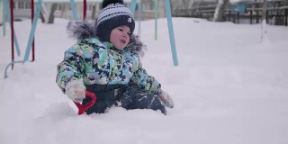 一个小孩在冬天的公园里玩雪。孩子拿着铁锹，在公园里积了很多雪。新鲜的空气里充满了乐趣和游戏。