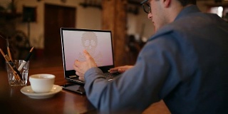 一名男子的笔记本电脑被一种勒索间谍病毒感染，该病毒要求支付赎金以获取加密文件。可怕的红色闪烁的头骨和交叉的骨头在屏幕上