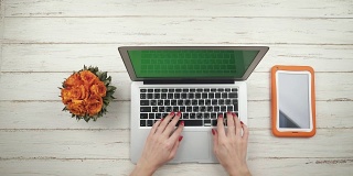 一位时髦的女士打开笔记本电脑，站在放着花的白色木桌上，输入文字，然后合上笔记本电脑。前视图。手关闭