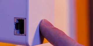 男子将手指按在WiFi中继器的WPS按钮上，该按钮位于墙上的电源插座上