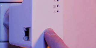 男子将手指按在WiFi中继器的WPS按钮上，该按钮位于墙上的电源插座上