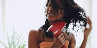 深色头发的女人用毛巾在家里用吹风机烘干头发