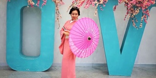 艺伎穿着粉红色的衣服在墙边走着，大爱带着樱花和转动着雨伞。
