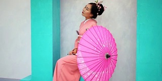 粉红色的艺妓坐在墙边，把伞烂掉了。