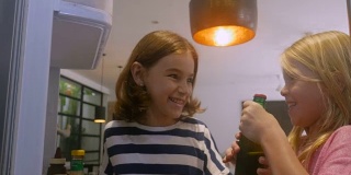 两个小女孩打开冰箱门，从冰箱里拿出一瓶绿色的汽水