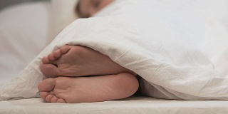女性在白毯子下挠脚，过敏需要治疗