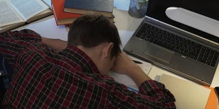 累男十几岁的学生一边做作业一边在桌子上睡觉，上学累了