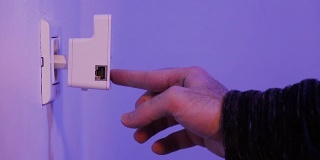 男子将WiFi中继器插入墙上的电源插座，然后用手指按WPS按钮