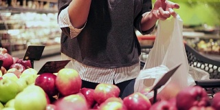 在杂货店挑选红苹果的女人。在超市的蔬果货架上，妇女用手挑选苹果