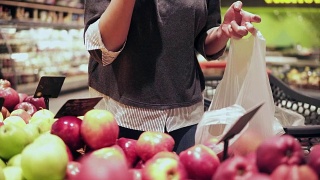 在杂货店挑选红苹果的女人。在超市的蔬果货架上，妇女用手挑选苹果视频素材模板下载