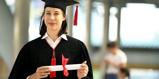 美丽的微笑毕业的学生女孩的肖像年轻的女人在帽子长袍行走和拿着文凭卷轴。