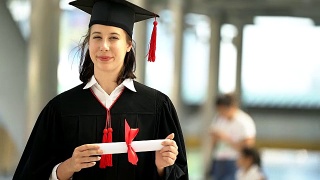 美丽的微笑毕业的学生女孩的肖像年轻的女人在帽子长袍行走和拿着文凭卷轴。视频素材模板下载