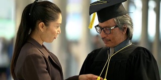 大四毕业生和他的妻子在准备毕业典礼的帽子长袍。