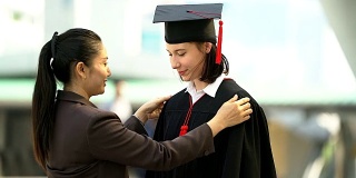 美丽的微笑毕业的学生女孩年轻的女人和她的母亲在帽子长袍准备毕业典礼。