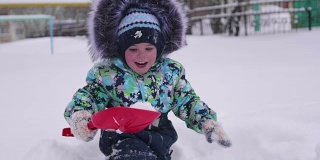 一个小孩在冬天的公园里玩雪。孩子拿着铁锹，在公园里积了很多雪。新鲜的空气里充满了乐趣和游戏。