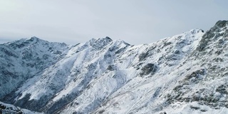 向前鸟瞰图在冬季雪山岩石山峰。落基山脉的峰顶被冰雪覆盖。冬季野外自然景观户外建立。全高清无人机飞行建立镜头