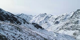 侧架空越过冬季雪山垭口，带着登山滑雪者向上攀登。冰雪覆盖的山顶和冰川。冬季野外自然户外建物。FullHD无人机飞行