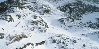 向前架空越过冬天的雪山，与登山的滑雪者一起向上攀登。冰雪覆盖的山顶和冰川。冬季野外自然户外建物。FullHD无人机飞行