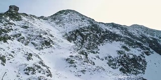 向后架空越过冬天的雪山，与登山滑雪者一起向上攀登。冰雪覆盖的山巅冰川。冬季野外自然户外建物。FullHD无人机飞行