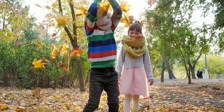 妹妹和弟弟在树的背景上向空中扔黄叶，在背光下玩耍