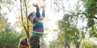 在秋天的公园里，欢快的孩子们在大自然的背光下玩耍，把黄叶抛向空中