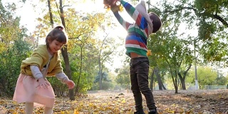 秋天的城市公园，孩子们在阳光下跳跃和扔树叶背景的树木和树叶