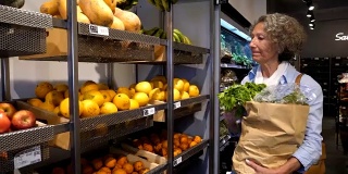 老妇人在有机食品市场购物，看着货架上食物的价格，然后选择水果